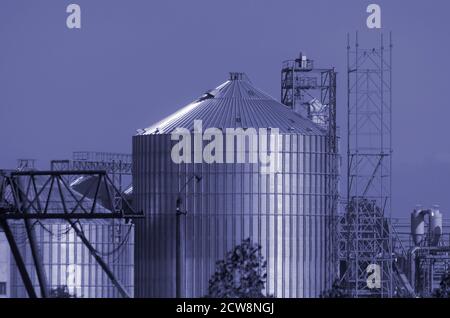 Costruzione di un moderno terminale di grano. Silo cilindrico metallico e struttura metallica di supporto per il trasportatore di carico. Agroalimentare. Foto a toni Foto Stock