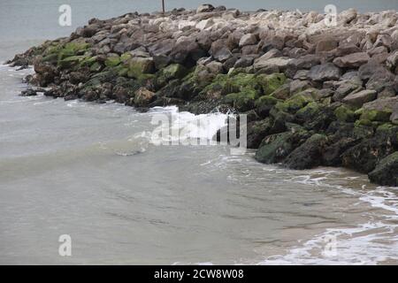 Onde lambiscono contro una groyne di pietra e roccia, progettato per fermare l'erosione e il movimento della spiaggia costiera, costa inglese del sud Foto Stock