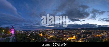 Luci cittadine di Graz e la famosa torre dell'orologio (Grazer Uhrturm) sulla collina di Shlossberg, Graz, regione della Stiria, Austria, dopo il tramonto. Vista panoramica. Foto Stock