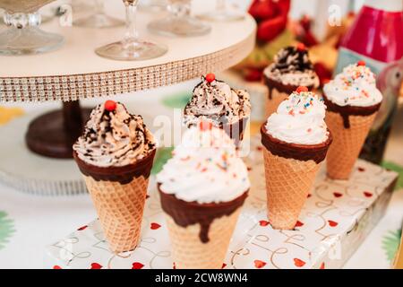 Coni di gelato con panna e spolverare su tavola dolce per il ricevimento di compleanno Foto Stock