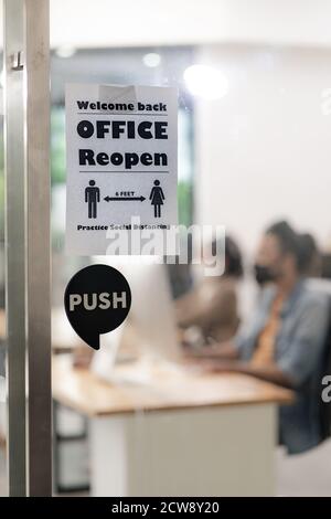 Insegne di Ufficio riaprono con pratica di divaricamento sociale con sfondo offuscato di squadra asiatica persone di affari che lavorano e indossare maschera viso in nuova norma Foto Stock