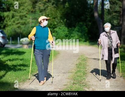 Due donne anziane che indossano maschere mediche che camminano con nordic walking poli durante la pandemia di covid-19 Foto Stock