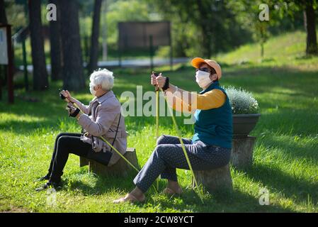Due donne anziane senior con maschere viso riposano dopo un Nordic walking durante la pandemia COVID-19 Foto Stock