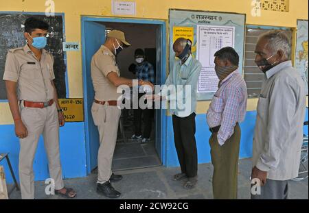 Beawar, Rajasthan, India, 28 settembre 2020: Gli elettori hanno le mani sanitizzate mentre aspettano di esprimere i loro voti per le elezioni di Panchayati Raj, in mezzo alla pandemia di coronavirus in corso, nel villaggio di Jhala ki Chauki vicino a Beawar. Oltre il 83.50 per cento degli elettori del 31.95-lakh hanno espresso i loro voti nella prima fase di 947 grammi Panchayat (Consiglio del Villaggio) elezioni in 25 distretti in tutto lo stato. Le linee guida relative al COVID-19 non sono state seguite durante le elezioni. Gli elettori indossano maschere facciali ma non hanno mantenuto la distanza sociale. Credit: Sumit Saraswat/Alamy Live News Foto Stock