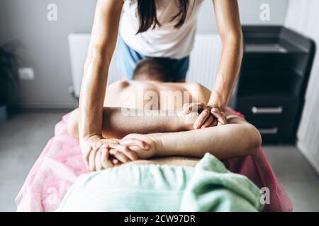 Una fisioterapista donna che fa massaggio alla schiena per un uomo in ufficio medico. Primo piano di mani che posano le mani del paziente dietro la schiena Foto Stock