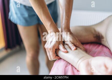 Una fisioterapista donna che fa massaggio alla schiena per un uomo in ufficio medico. Primo piano del riscaldamento della mano del paziente. Foto Stock