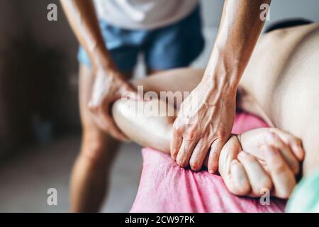 Una fisioterapista donna che fa massaggio alla schiena per un uomo in ufficio medico. Primo piano del riscaldamento della mano del paziente. Foto Stock