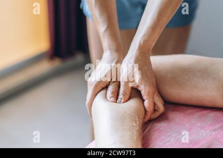 Una fisioterapista donna che fa massaggio alla schiena per un uomo in ufficio medico. Primo piano del riscaldamento della mano del paziente. Foto Stock