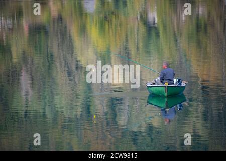 Riflessi e riflessi sull'acqua del lago in autunno. Pescatore in una piccola barca Foto Stock