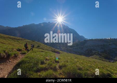 Uomo e donna su un sentiero nelle Dolomiti, in mezzo a un prato fiorito e in una magnifica giornata di sole. Concetto: Divertimento e vacanza in montagna, salute Foto Stock