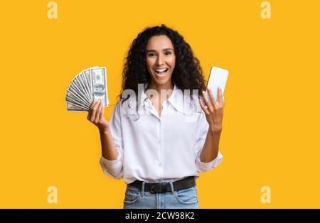 Concetto di cashback. Smartphone di Young Woman Holding e Dollar Cash eccitati Foto Stock