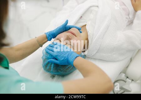 Cosmetoligist fare il massaggio del viso in salone di bellezza. Preparazione per l'iniezione. Cosmetologo in maschera medica protettiva Foto Stock