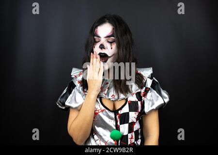 donna in un costume di clown halloween su sfondo nero isolato molto sonnolento e stanco Foto Stock