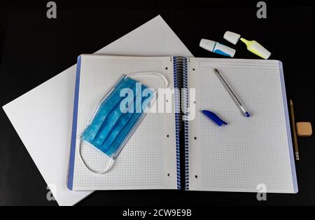 Materiale scolastico e maschera protettiva su sfondo nero, di nuovo a scuola dopo la pandemia Foto Stock