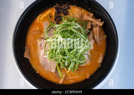 Vista dall'alto di una grande ciotola di ramen piccante di chashu sormontata da germogli di bambù con delicata presentazione per servire. Foto Stock