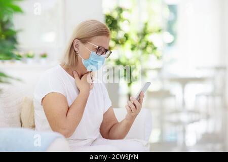 Donna malata in maschera facciale che chiama medico. Videochat online e teleconferenza con il personale medico dell'ospedale. Tosse da pazienti anziani malati. Coronavirus ou Foto Stock