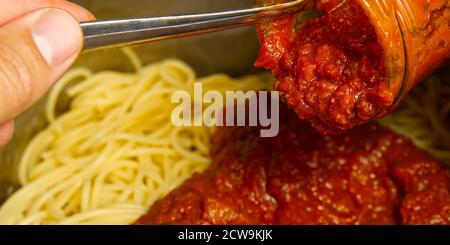 Aggiungere la salsa bolognese sugli spaghetti in pentola e cuocere la pasta bolognese a casa Foto Stock