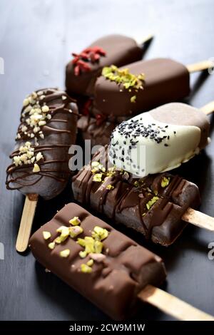 Uno scatto ravvicinato che mostra le mani di uno chef che decora una gelateria gourmet al cioccolato. Il dessert è immerso nel cioccolato fondente e cosparso di Foto Stock