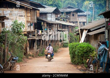 Un piccolo villaggio rurale, un villaggio di tribù collina a Chiang mai Thailandia, case in legno e bambù, e una strada sterrata con una moto. Foto Stock