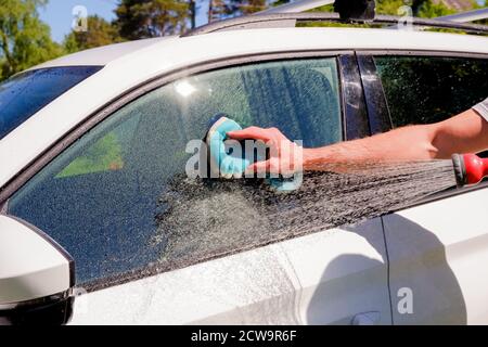 Lavaggio auto bianco su open air.Male mani tenere con spugna blu lavaggio car.SOAP suds, bolle e mitt. Foto Stock