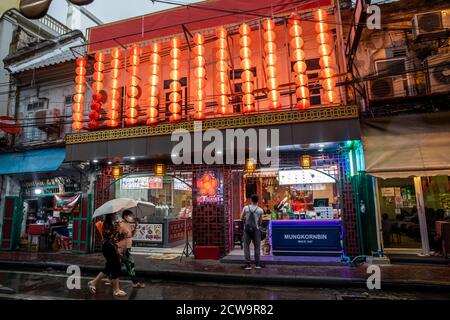 Una coppia cammina sotto gli ombrelloni mentre un altro uomo guarda in un ristorante a Chinatown di Bangkok. Foto Stock