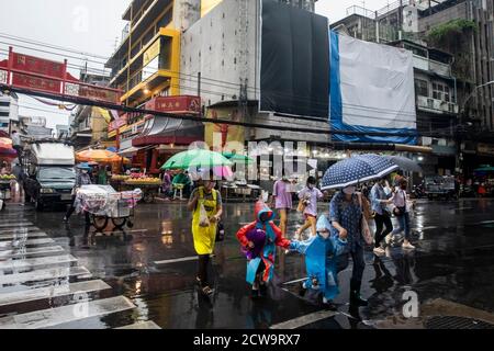 I genitori e i bambini piccoli scamper per tutta la strada sotto la pioggia per fare luce verde durante una giornata piovosa nella Chinatown di Bangkok. Foto Stock