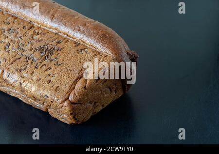 Pagnotta di pane di segale con semi di cumulo su fondo nero. Vista laterale del pane fatto in casa appena sfornato cosparso di semi di cumino. Spazio di copia. Selectiv Foto Stock