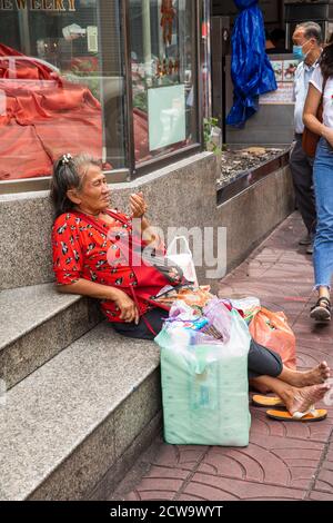 La vecchia donna che sembra senza casa siede all'ingresso di un edificio nella Chinatown di Bangkok. Foto Stock