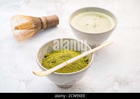 Polvere di tè verde Matcha con spazzola di whisk di bambù Matcha su fondo di cemento bianco . Foto Stock