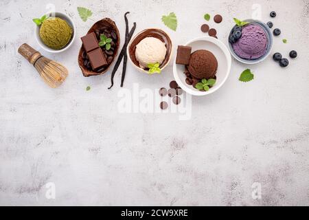 Vari gusti di gelato in ciotola mirtillo, tè verde, cocco e cioccolato impostazione su sfondo di pietra bianca. Foto Stock