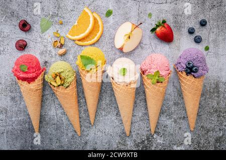 Vari gusti di gelato in coni di mirtillo, tè verde, pistacchio, mandorla, arancio e ciliegia impostazione su fondo di pietra scuro. Menu estivo e dolce Foto Stock