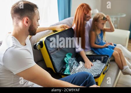 felice giovane famiglia caucasica pronta a viaggiare, concetto di viaggio, eccitati genitori e bambina sedersi sul divano, imballaggio bagagli Foto Stock