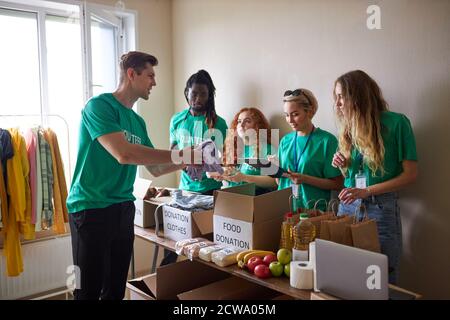 diversi volontari si impacchettano, raccolgono gli aiuti umanitari nella scatola delle donazioni. gruppo multietnico di persone che lavorano in fondazione caritativa per aiutare in crisi e senza tetto Foto Stock