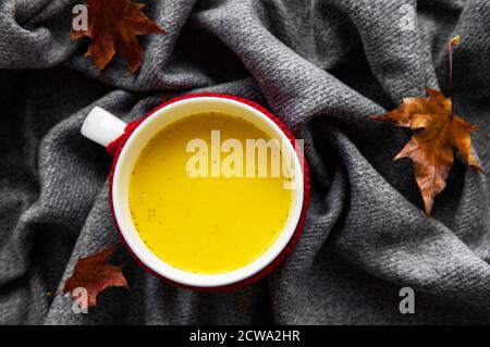 Latte dorato in una tazza bianca. Foglie d'autunno. Una bevanda sana a base di latte, curcuma, cannella e miele. Foto Stock
