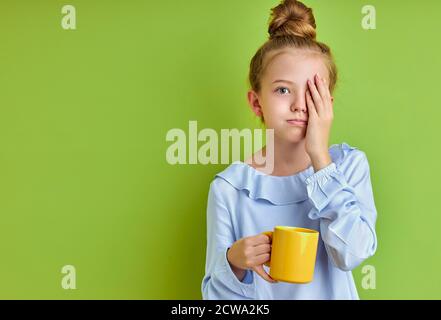 sonnolenta bambina non ha abbastanza sonno la mattina prima di scuola, lei sta tenendo una tazza di caffè, stanca Foto Stock