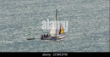 Portland Harbour, UK - 2 luglio 2020: barca a vela bianca nel porto. Piccola barca di salvataggio che tagga lungo. Foto Stock