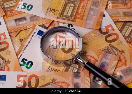 Un sacco di 50 banconote in euro sparse su un tavolo, con una lente d'ingrandimento. Foto Stock