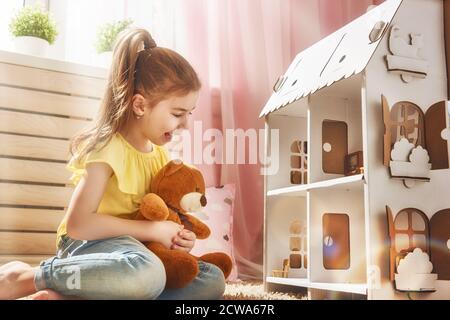 La ragazza felice gioca con la casa della bambola e l'orso del teddy a casa. Divertente, il bambino adorabile si diverte nella camera dei bambini. Foto Stock