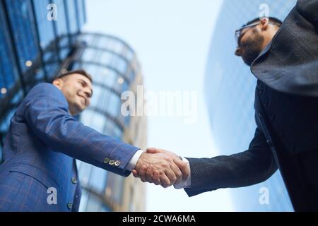 Vista ad angolo basso di due giovani uomini d'affari che scuotono le mani durante il loro incontro in città Foto Stock