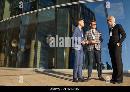 I colleghi di lavoro si comunicano tra loro mentre si trovano nelle vicinanze di ingresso all'esterno dell'edificio per uffici Foto Stock