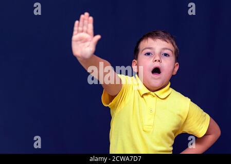 Giovane caucasico a bocca aperta 9 s ragazzo mettendo la mano fuori facendo segno di stop Gesture.Blue sfondo studio. Foto Stock