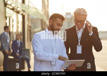 Una coppia aziendale multietnica che lavora online su un tablet digitale insieme in piedi all'aperto Foto Stock