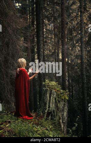 Donna con mantello rosso in preghiera nella foresta Foto Stock
