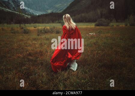 Donna con mantello rosso che corre in una terra desolata Foto Stock