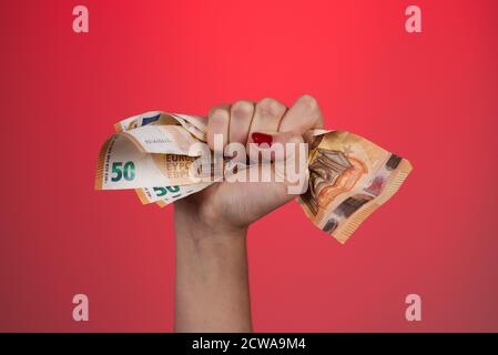 Una mano femminile che contiene diverse banconote da 50 euro. Sfondo rosso. Spazio di copia. Foto Stock