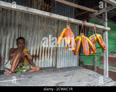 Isola di Ambon, Indonesia - 11 febbraio 2018: Un uomo vende una grande banana arancione. Le banane sono appese in una bancarella di mercato in una piccola città sull'isola di Ambon, Foto Stock