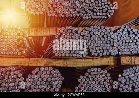 Stoccaggio e impilamento di file di barre rotonde in acciaio nel magazzino per l'edilizia industriale. Bianco e nero con messa a fuoco superficiale. Foto Stock