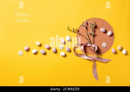 Biglietto di auguri di Pasqua con rami salici in fiore, caramelle colorate su sfondo giallo arancio brillante. Iscrizione buona Pasqua. Disposizione piatta, spazio di copia Foto Stock