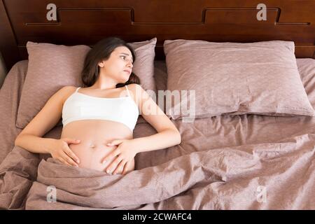 bella giovane donna incinta sdraiata a letto, vista dall'alto. la ragazza soffre del fatto che suo marito la ha lasciata, Foto Stock