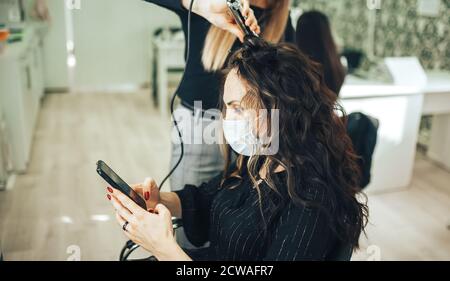 Donna in maschera medica ottiene i suoi capelli fatti in bellezza salone durante la pandemia Foto Stock